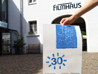 Eine Hand hält das Jubiläumsplakat im Filmhaus-Innenhof hoch